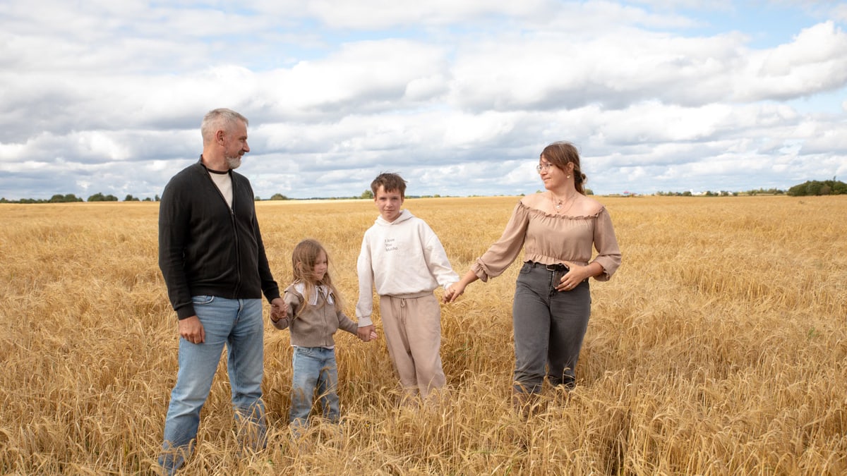Happy family walking hand in hand through a golden wheat field on a sunny day.